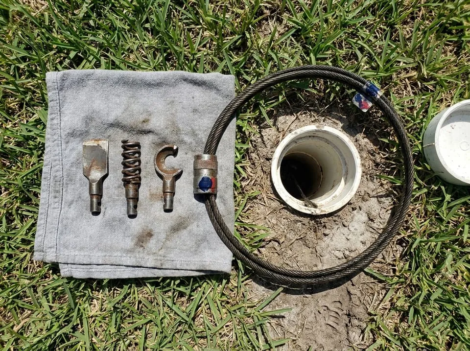 Cable cutter heads laid on a rag beside an open cleanout before main sewer line cleaning in a Florida yard